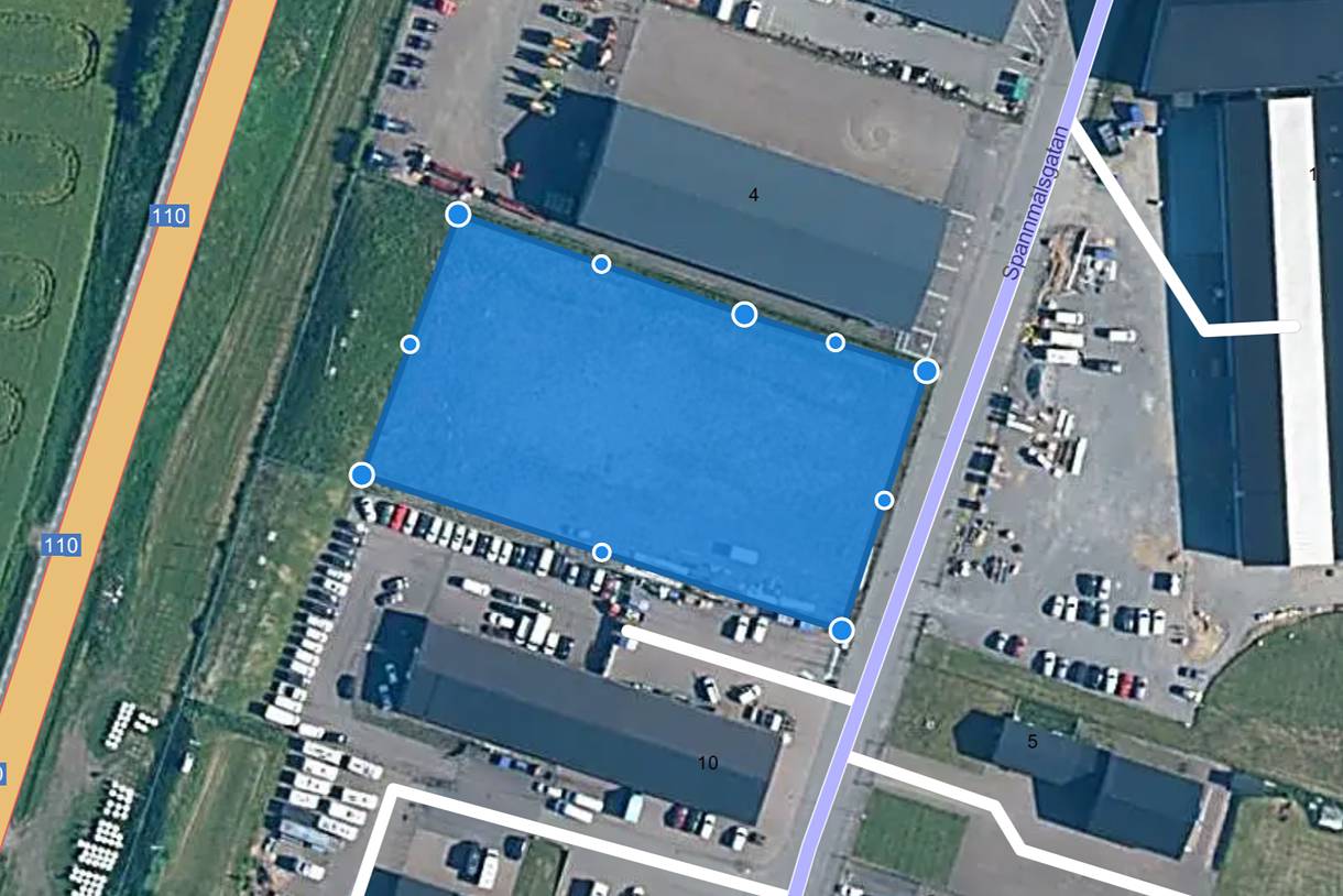 Flygbild över industriområdet med tomten markerad i blått och industribyggnader på båda sidor om den.