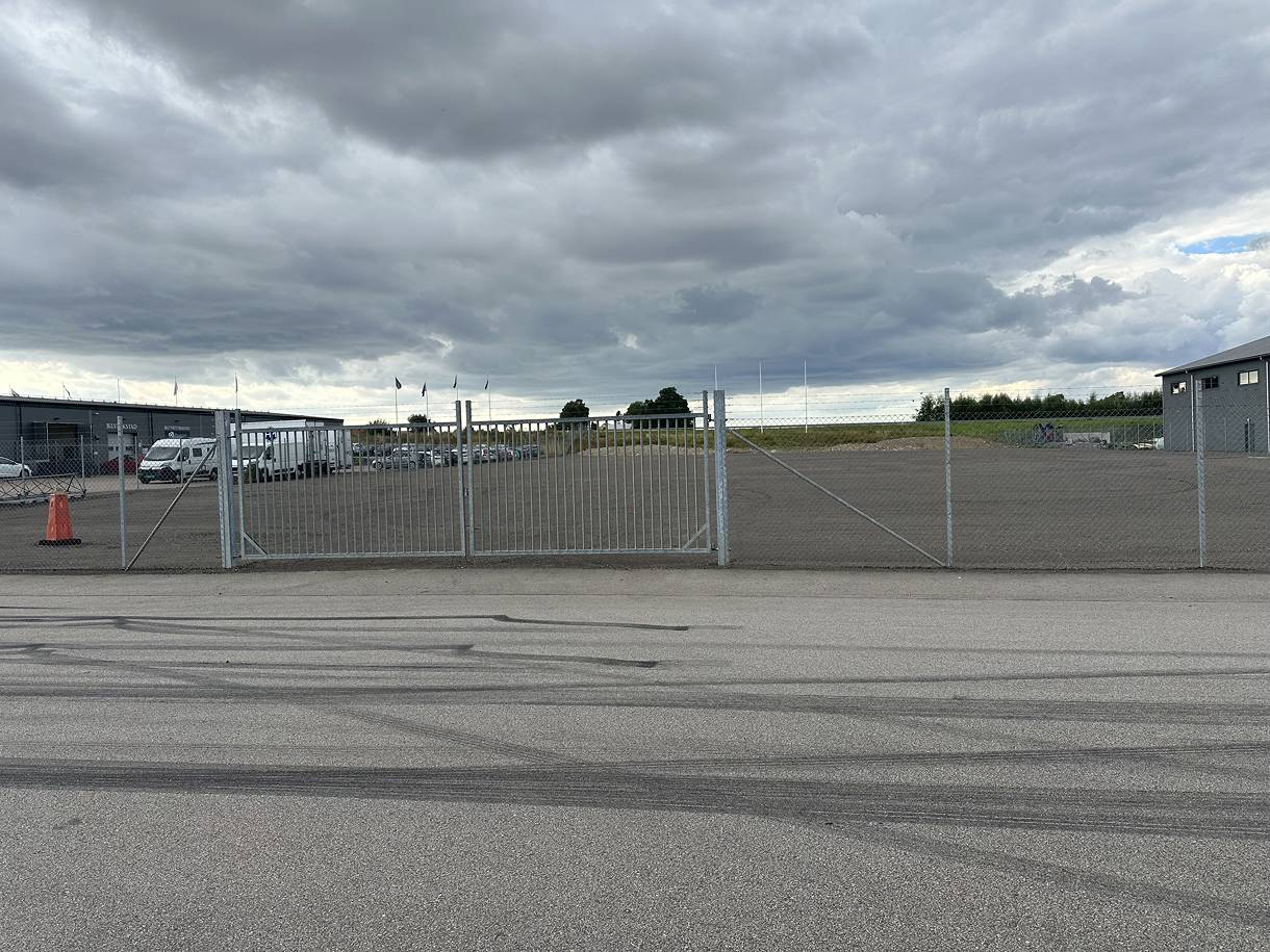 Den breda dubbelgrinden in till tomten, sedd från gatan. Innanför ligger den hårdgjorda ytan.